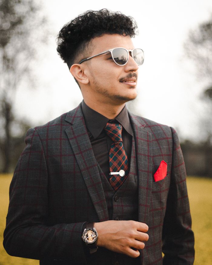 Portrait of a fashionable man with sunglasses in a checkered suit, standing confidently outdoors.