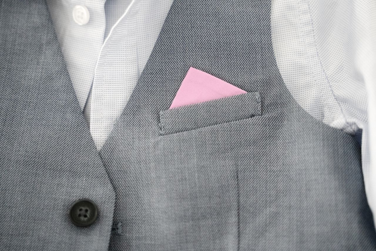 Close-up of a gray vest featuring a pink pocket square, showcasing elegant fashion style.