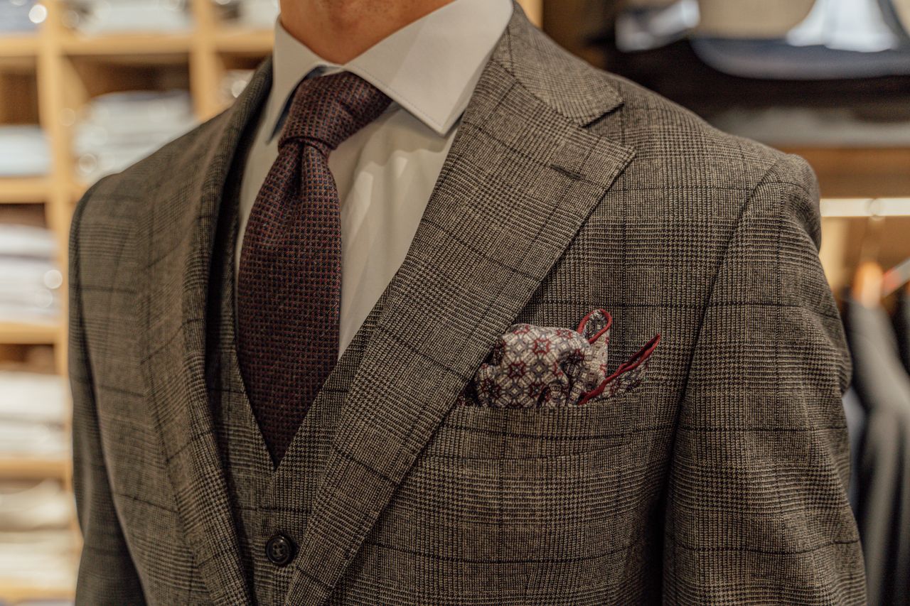 who-we-are Close-up of a tailored suit showcased in a fashion boutique, highlighting intricate patterns and style.